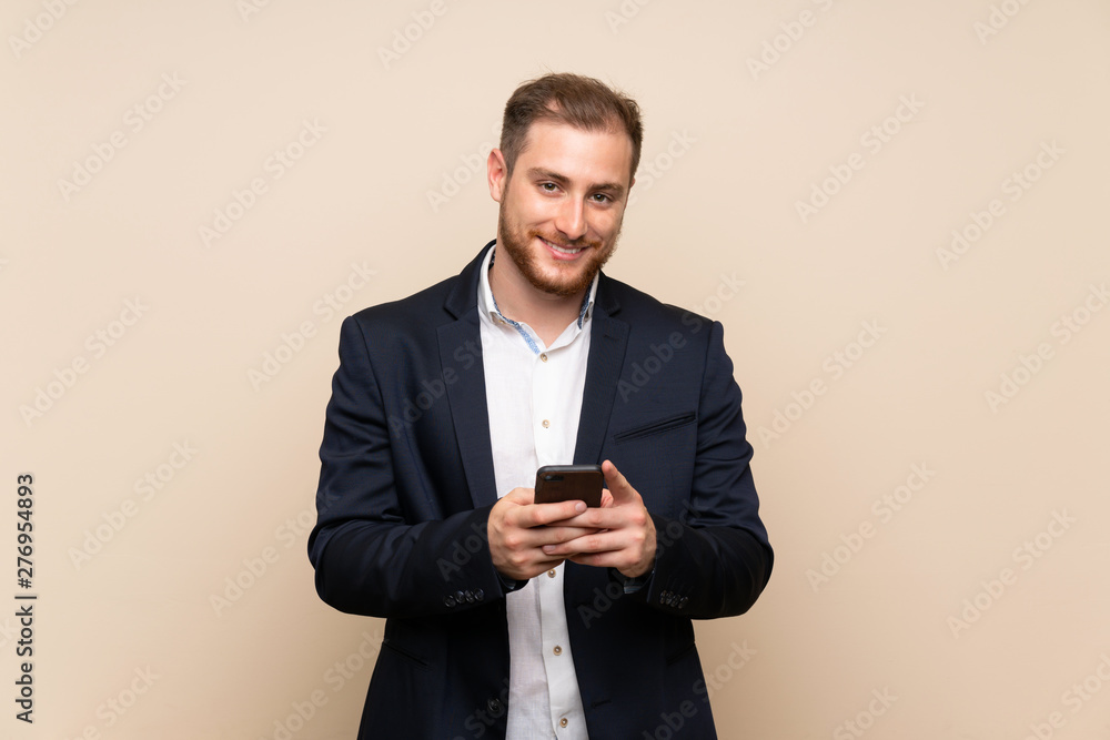 Blonde man over isolated background sending a message with the mobile Blonde man over isolated background sending a message with the mobile