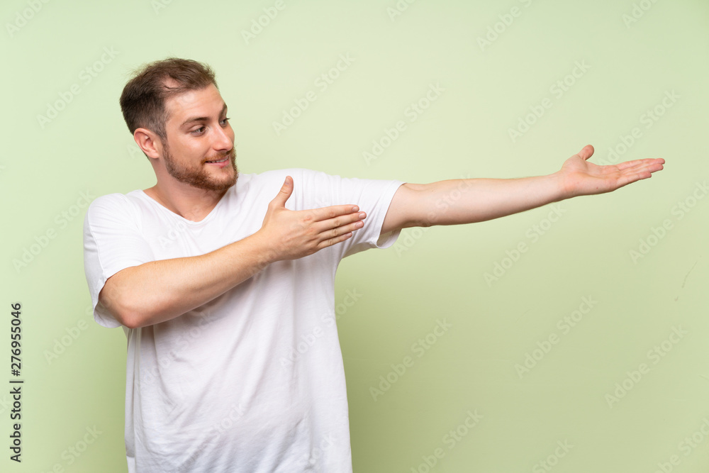 Handsome man over green background extending hands to the side for inviting to come Handsome man over green background extending hands to the side for inviting to come