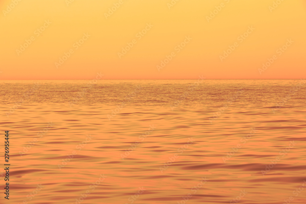 Fototapeta premium Abstract horizontal theme by means of waves, water, skyline, and sky during golden sunset. Soft pastel detail of sea waves. Out of focus and blurred. Soft focus