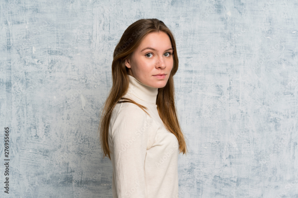 Young woman over grunge wall keeping arms crossed and looking side Young woman over grunge wall keeping arms crossed and looking side
