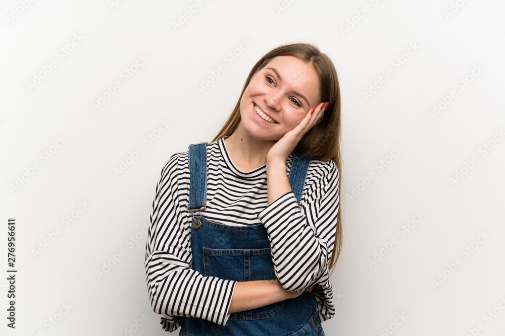 Fototapeta premium Young woman in dungarees over white wall laughing