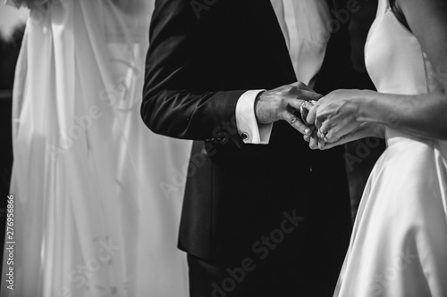 A bride and a groom are putting the rings on each others fingers. Black and white image.