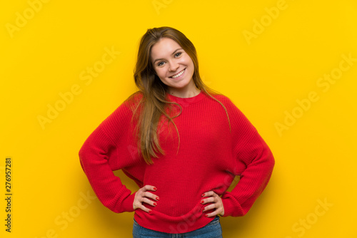 Young woman over yellow wall posing with arms at hip and smiling