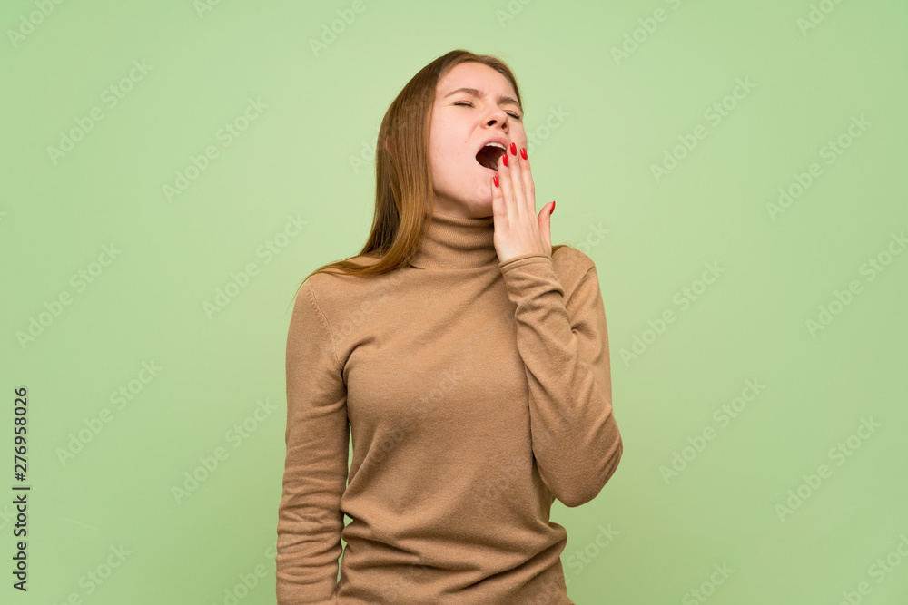 Young woman with turtleneck sweater yawning and covering wide open mouth with hand Young woman with turtleneck sweater yawning and covering wide open mouth with hand