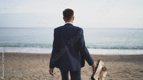 A man in a business suit is walking along the beach towards the sea photo