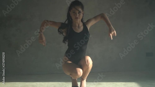 Beautiful sensual woman in black body suit dancing in hazy studio with grey concrete walls - video in slow motion