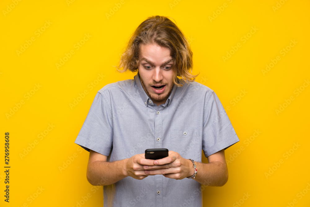 Blonde man over isolated yellow background surprised and sending a message Blonde man over isolated yellow background surprised and sending a message