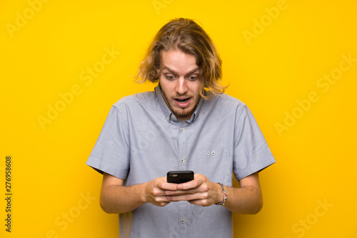 Blonde man over isolated yellow background surprised and sending a message © luismolinero