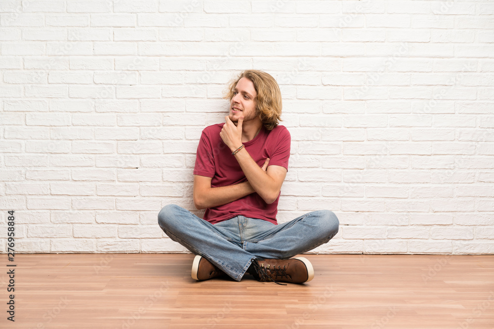 Blonde man sitting on the floor looking to the side Blonde man sitting on the floor looking to the side