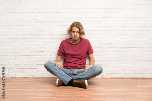Blonde man sitting on the floor with sad and depressed expression © luismolinero