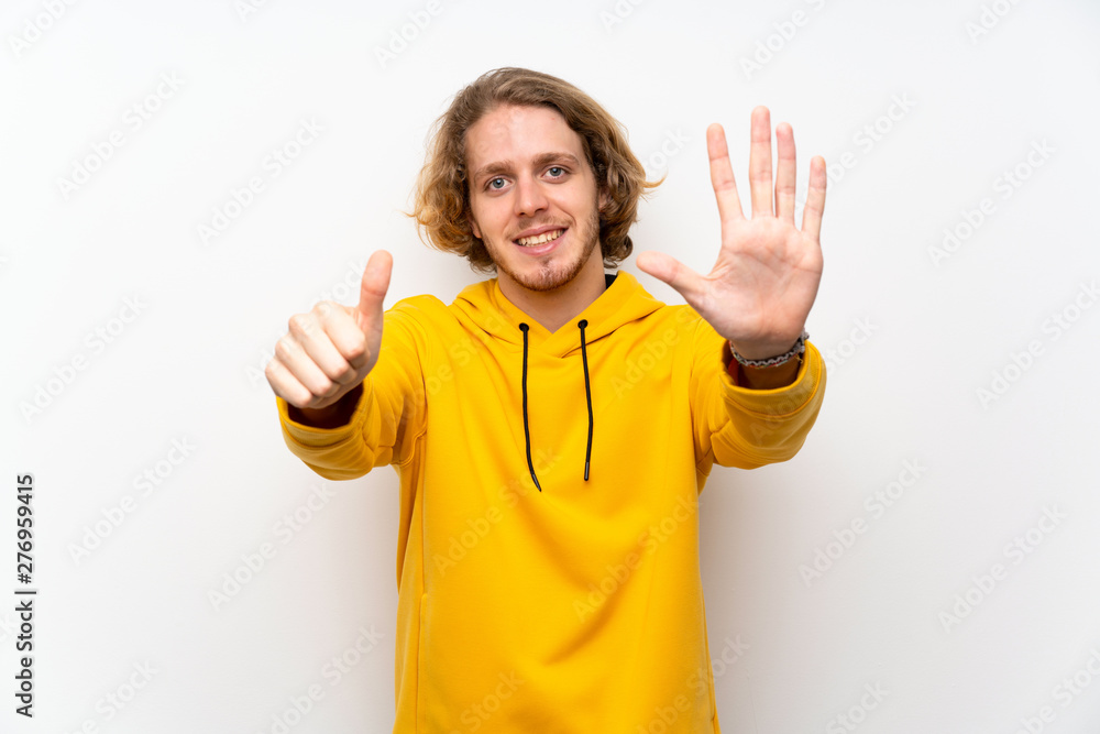 Blonde man with sweatshirt over white wall counting six with fingers Blonde man with sweatshirt over white wall counting six with fingers