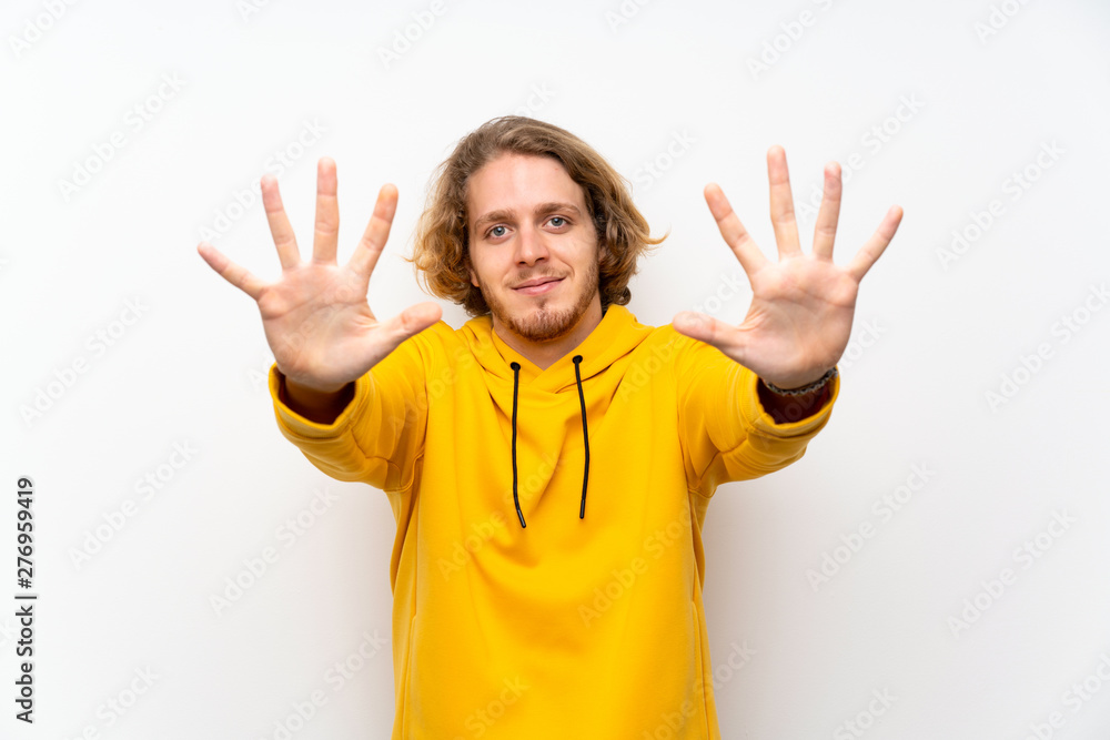 Blonde man with sweatshirt over white wall counting ten with fingers Blonde man with sweatshirt over white wall counting ten with fingers