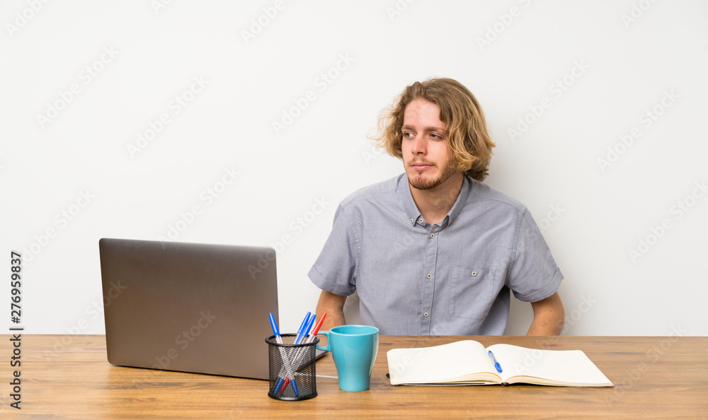 Blonde man with a laptop making doubts gesture looking side Blonde man with a laptop making doubts gesture looking side