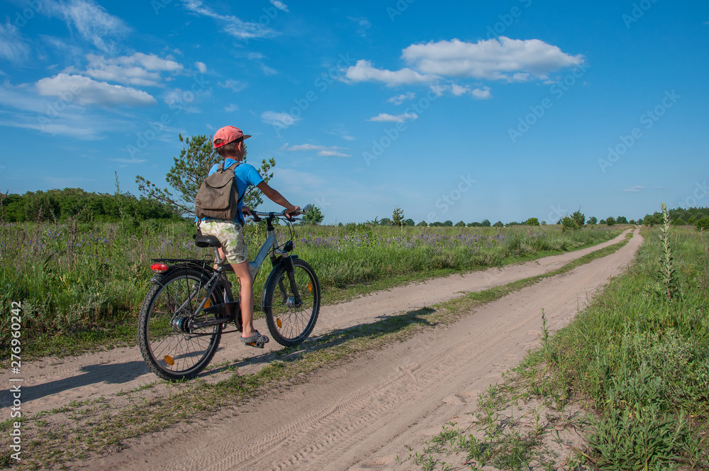 Obraz premium Seven-year-old boy on a sports bike rides along a dirt road against blue sky