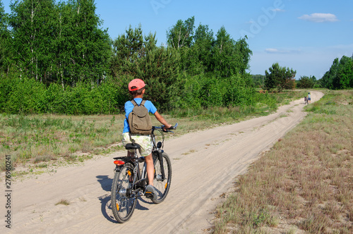 Seven-year-old boy on a sports bike rides along a dirt road against blue sky