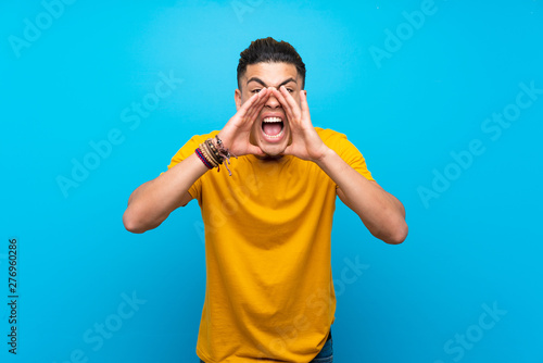Young man with yellow shirt over isolated blue background shouting and announcing something
