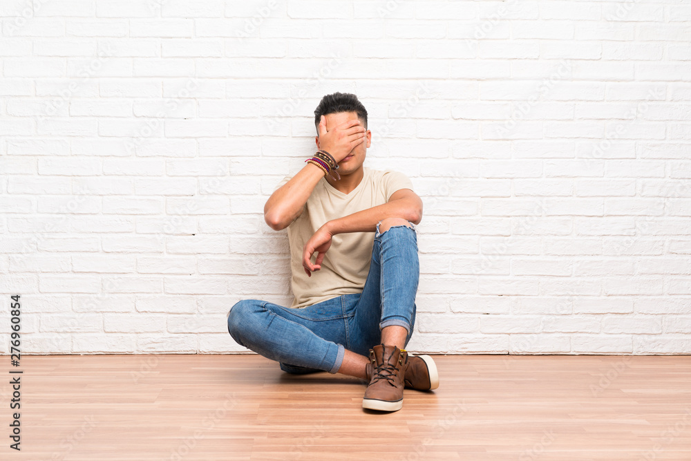 Young man sitting on the floor covering eyes by hands