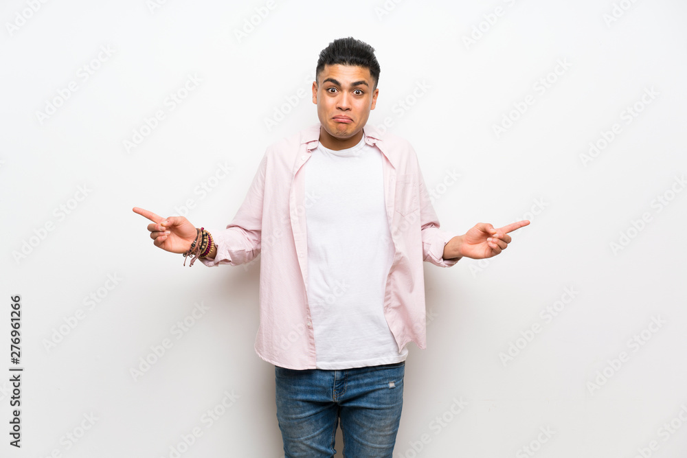 Young man over isolated white wall pointing to the laterals having doubts Young man over isolated white wall pointing to the laterals having doubts