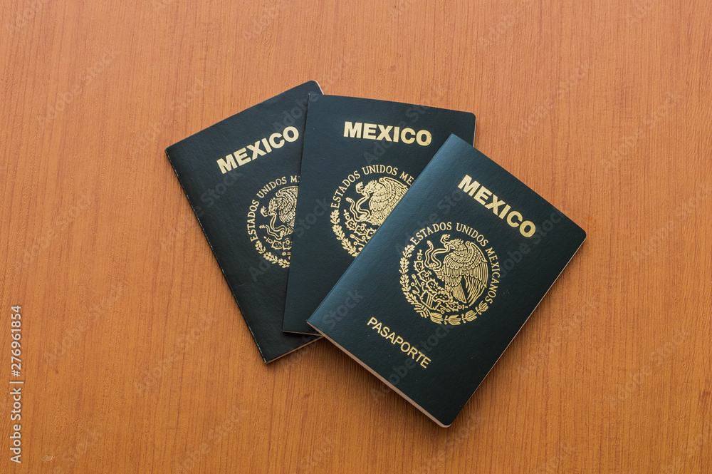 Tres pasaportes mexicanos apilados sobre mesa de madera. Vista desde arriba.