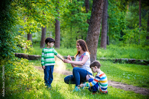 Obraz na plátne Young woman mother applying insect repellent to her two son before forest hike beautiful summer day or evening