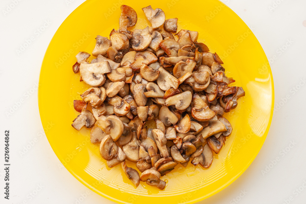 Mushrooms champignons on the yellow plate on the white table Mushrooms champignons on the yellow plate on the white table