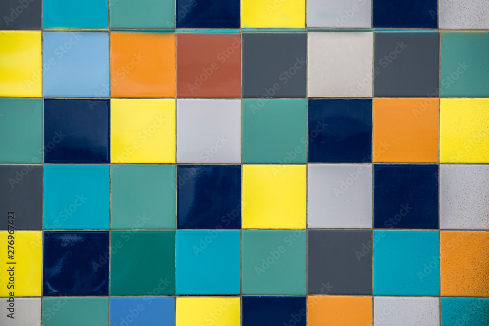 wall of bright multi-colored yellow, blue, white, gray square ceramic tiles. rough surface texture