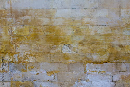 old damaged gray wall of large bricks with bright yellow spots of paint. rough surface texture