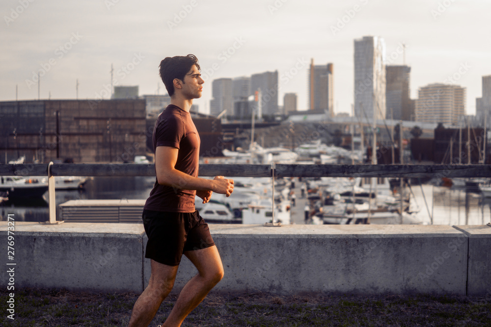 Young athletic man running at park with skyscrapers on background. Urban run