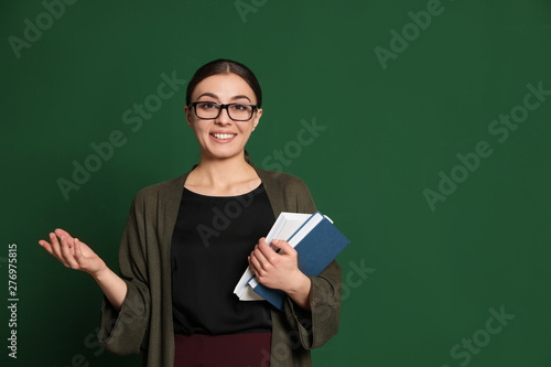 Portrait of young teacher with books on green background. Space for text