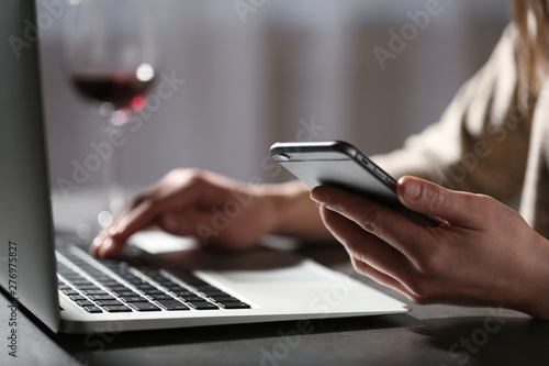 Woman using smartphone and laptop at table indoors, closeup. Loneliness concept