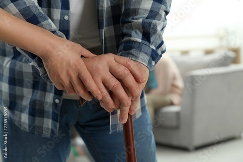 Nurse assisting elderly man with cane indoors, closeup. Space for text