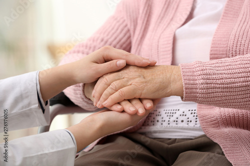 Nurse holding hands of elderly woman against blurred background, closeup. Assisting senior generation © New Africa
