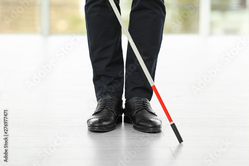 Blind person with long cane standing indoors, closeup