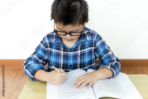 Little student boy in glasses doing his homework on the table with white background