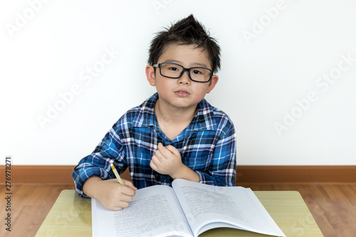 Little student boy in glasses doing his homework on the table with white background