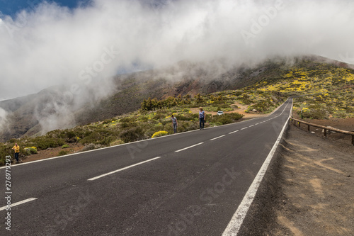 Modern road, runs along the streams of frozen lava and surrounded by mountain vegetation, rests on the clouds, flowing into the caldera valley.. National Park Teide, Tenerife, Canary Islands, Spain photo