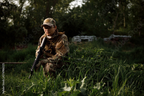 Airsoft soldier in full ammunition with rifle playing strikeball in outdoor in grass
