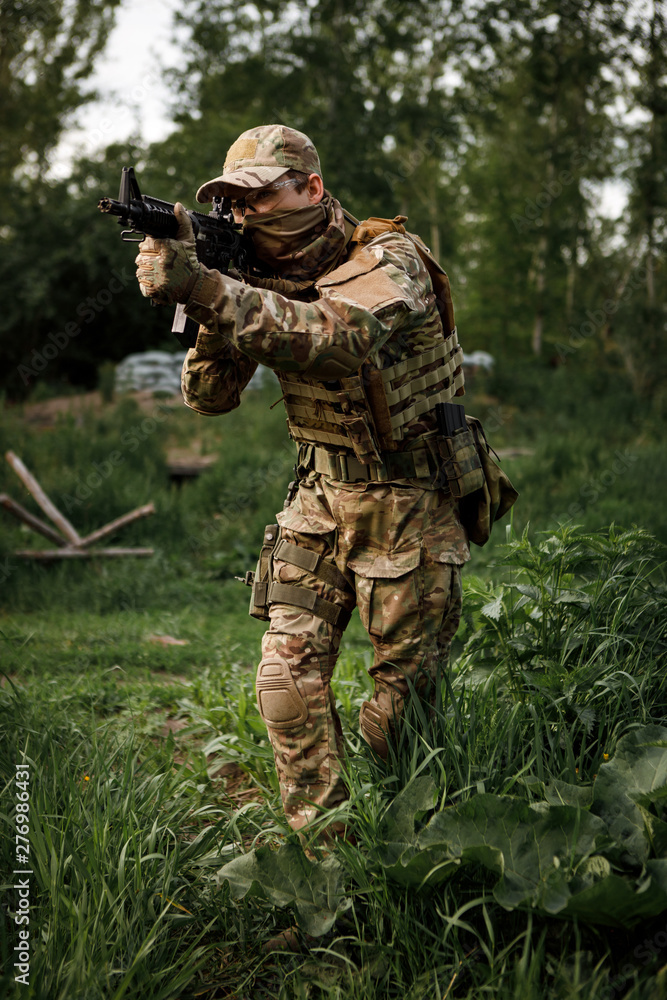 Airsoft soldier in full ammunition with rifle playing strikeball in outdoor in grass