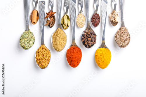 Various spices ( cumin, coriander, curry, paprika, chili, turmeric cinnamon, fenugreek, cardamom, basil leaf, parsley, cloves ) in spoons on white background. Top view with copy space.