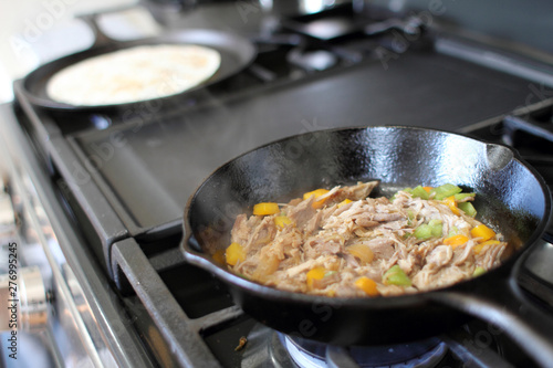 Mexican style pulled pork, known as carnitas, cooking in a cast iron skillet with a flour tortilla on a camal skillet.