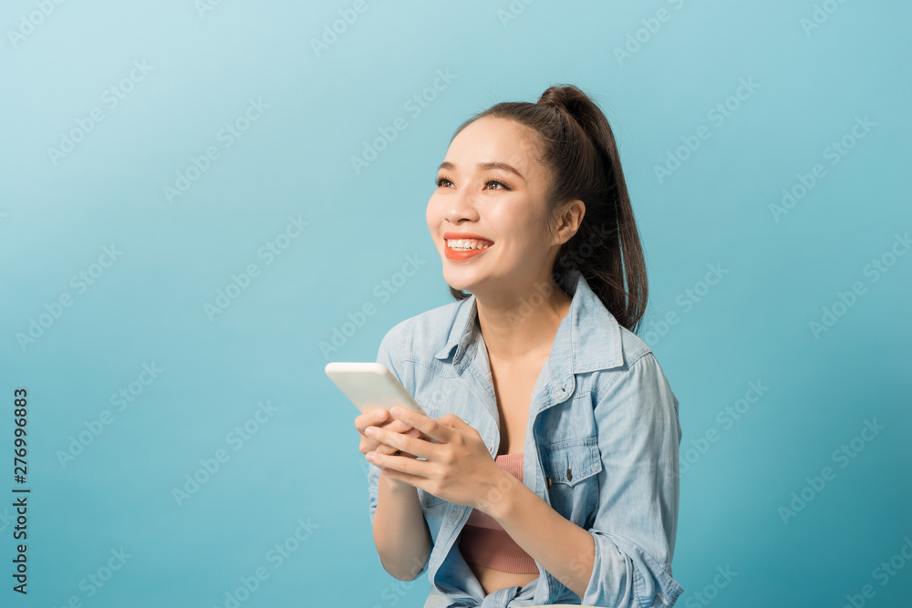 Asian woman 20s holding mobile phone and smiling over blue background Asian woman 20s holding mobile phone and smiling over blue background