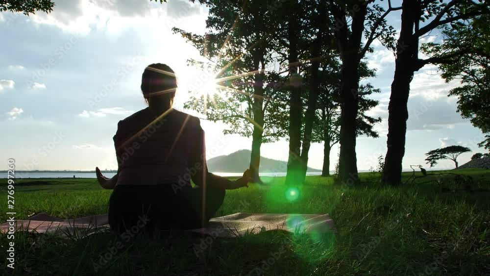Asian women practicing yoga relax in nature in the evening sunlight, Lotus pose on meditation session. Fitness and healthy lifestyle concept. Slow motion Asian women practicing yoga relax in nature in the evening sunlight, Lotus pose on meditation session. Fitness and healthy lifestyle concept. Slow motion