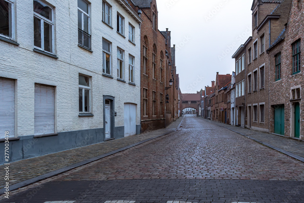 Picturesque old street of Bruges with traditional medieval houses and cobbled road in slight morning fog. Cityscape of Bruges streets.