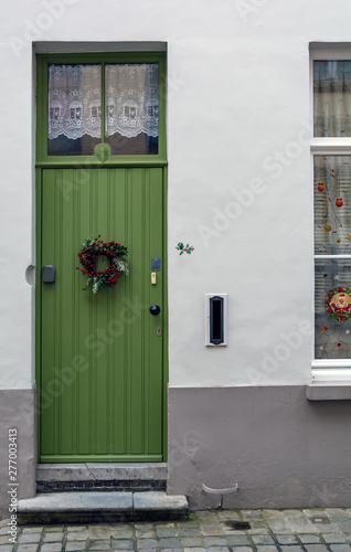Vintage green front door decorated with Christmas wreath shot in Bruges, Belgium. Old green door with window at the top.