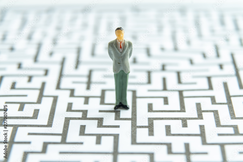 Miniature people: Businessman standing on start point of maze Miniature people: Businessman standing on start point of maze