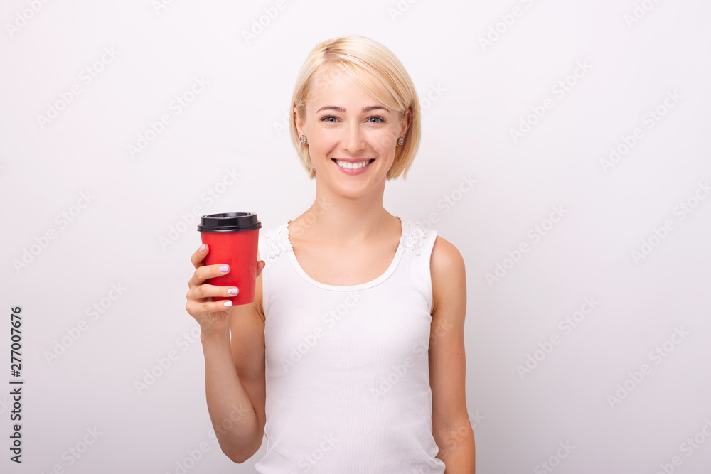 Cheerful young woman, looking at camera with toothy smile, while holding a red cup of coffee, over isolated background Cheerful young woman, looking at camera with toothy smile, while holding a red cup of coffee, over isolated background