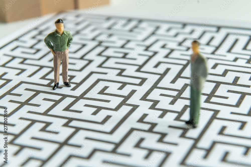 Miniature people: Businessman standing on start point of maze Miniature people: Businessman standing on start point of maze