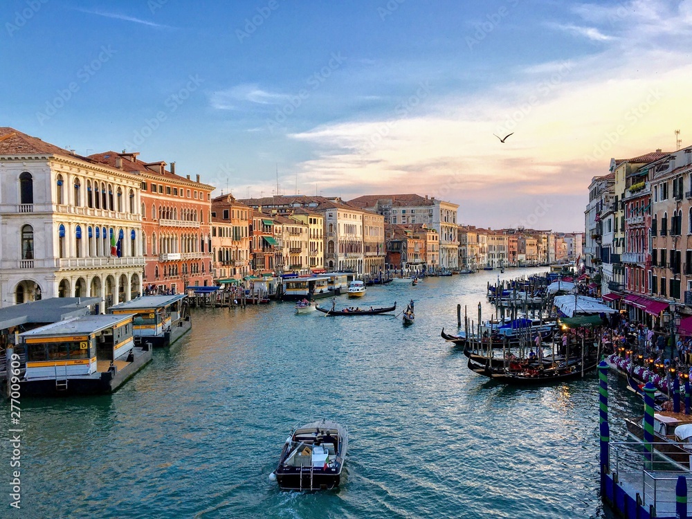 A view of the Grand Canal from the Rialto Bridge in Venice, Italy.  It is a busy summer evening with a water taxi driving down the middle of the canal past gondolas.