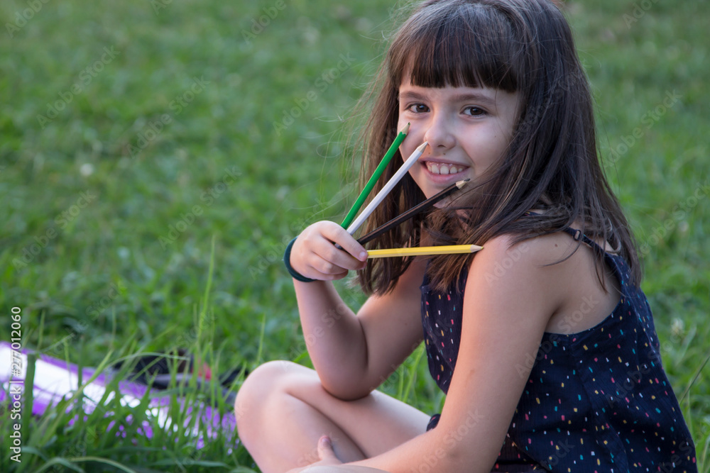 girl sitting with colored pencils and notebook on the grass, concept of college and education girl sitting with colored pencils and notebook on the grass, concept of college and education