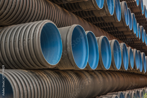 Large black PVC pipes for industrial use are neatly stacked, many round tubular materials photo